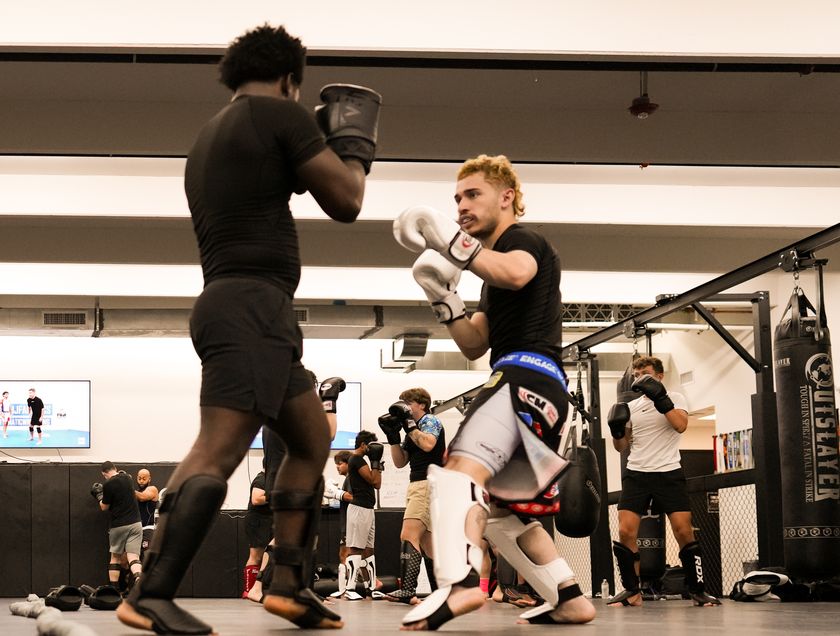 Two adults drill Muay Thai pad work in the gym.