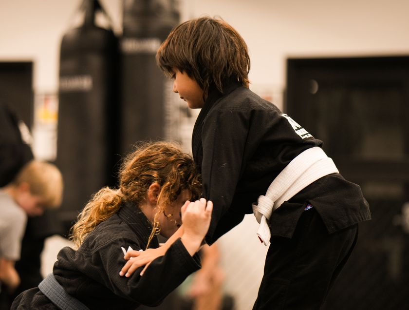 Two kids in gis practise a jiu-jitsu takedown.